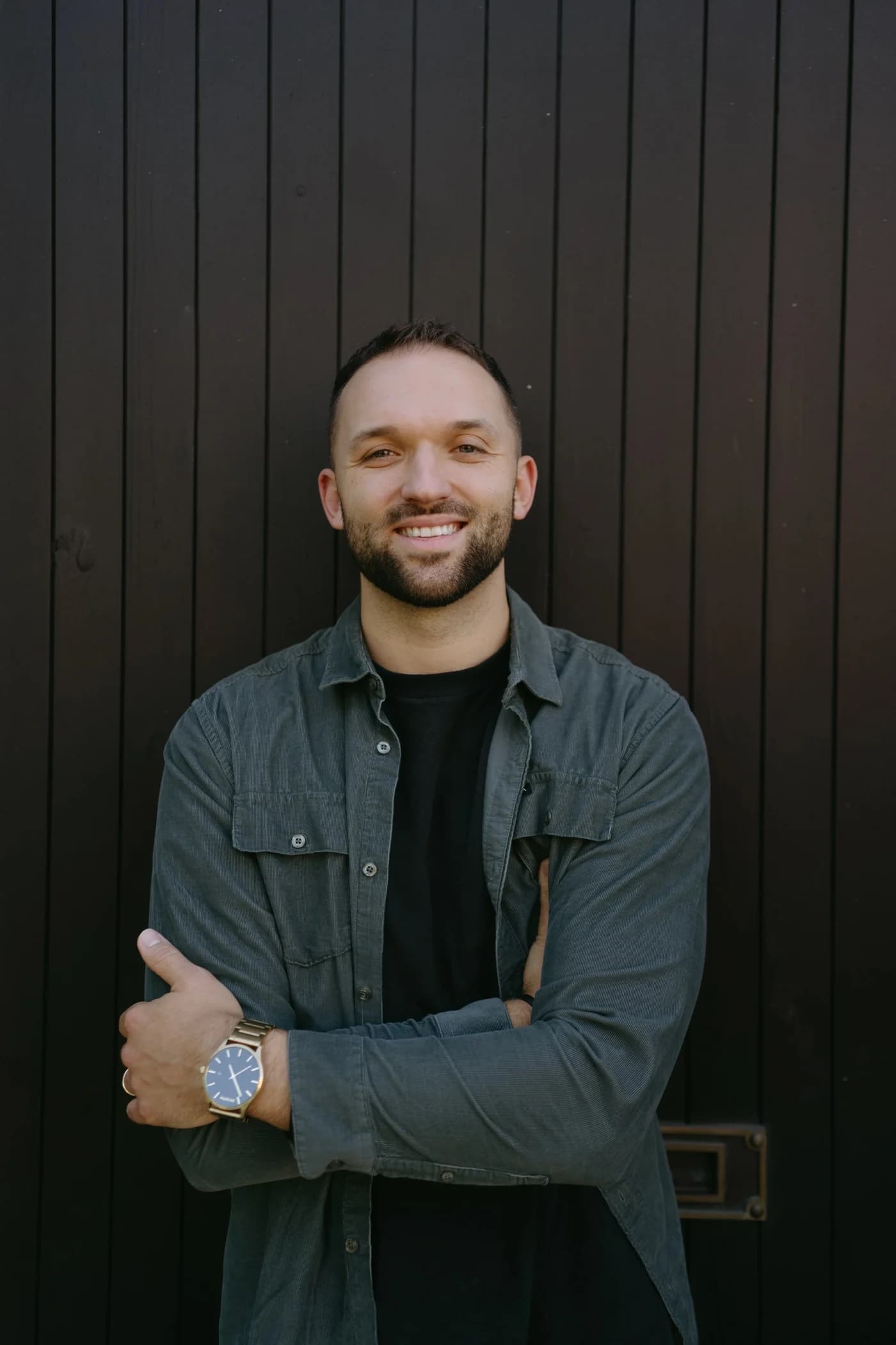 Kyle Hoffman smiling with arms crossed against a dark wood wall